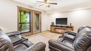Una sala de estar con cómodos sofás reclinables de cuero, un televisor de pantalla plana, chimenea y ventilador de techo.