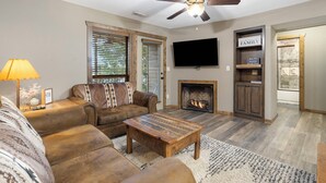 A living room with a brown leather sofa, a wooden coffee table, a fireplace, and a television mounted on the wall. - Lakefront Condo, Private Deck, Sleeps 12. 4 bedroom, 3 Bathroom.  2 miles from Siilver Dollar City (Branson)