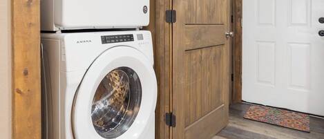 A laundry room with two stacked washing machines, wooden doors, and a patterned mat.