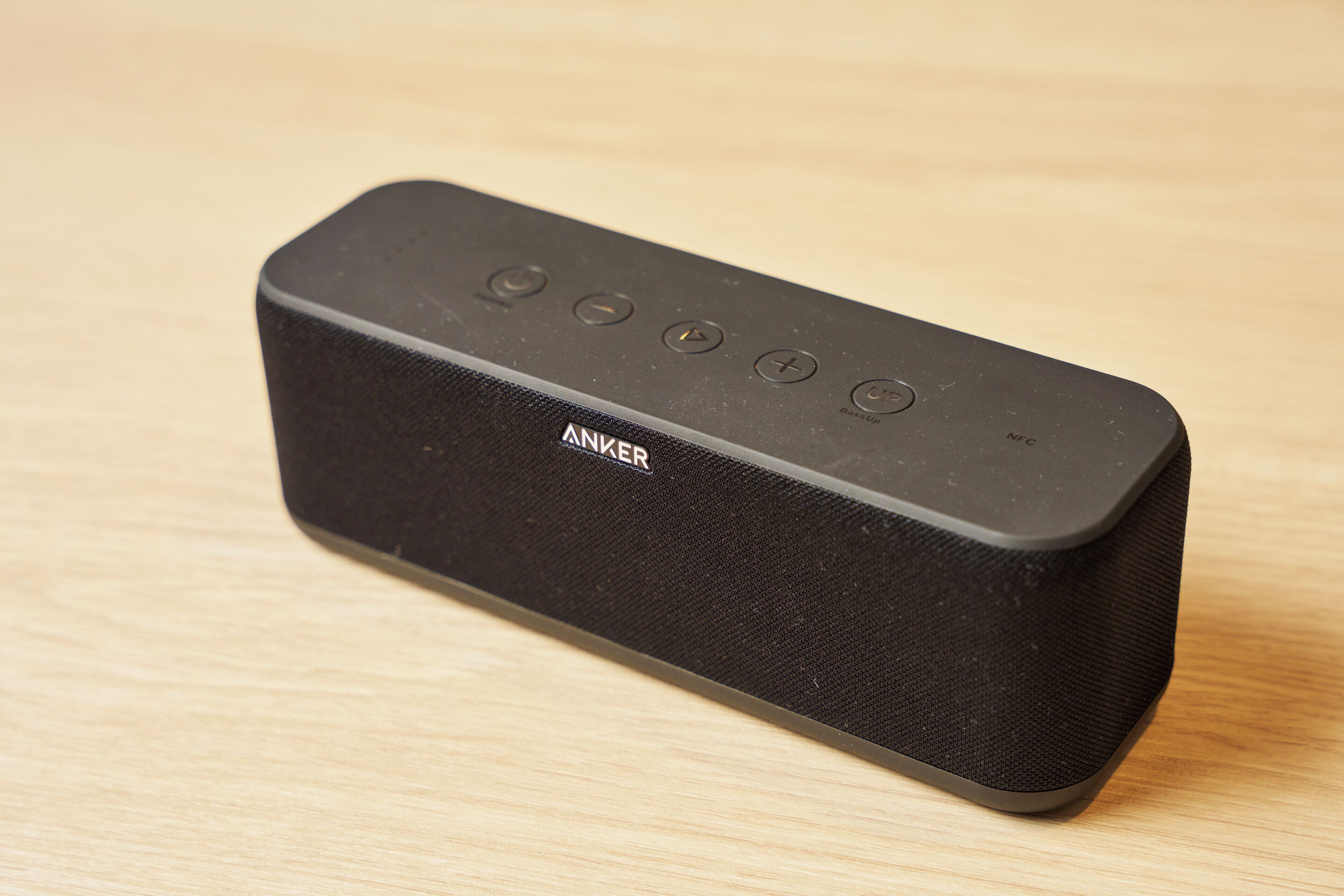 A black portable speaker with a fabric texture and a brand name visible on the side.