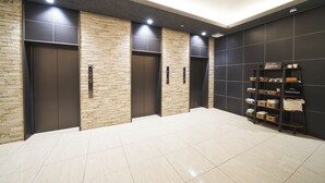 A modern elevator area with three elevators, a tiled floor, and a shelf with bags and boxes. - KOKO HOTEL Osaka Namba Sennichimae (Osaka)