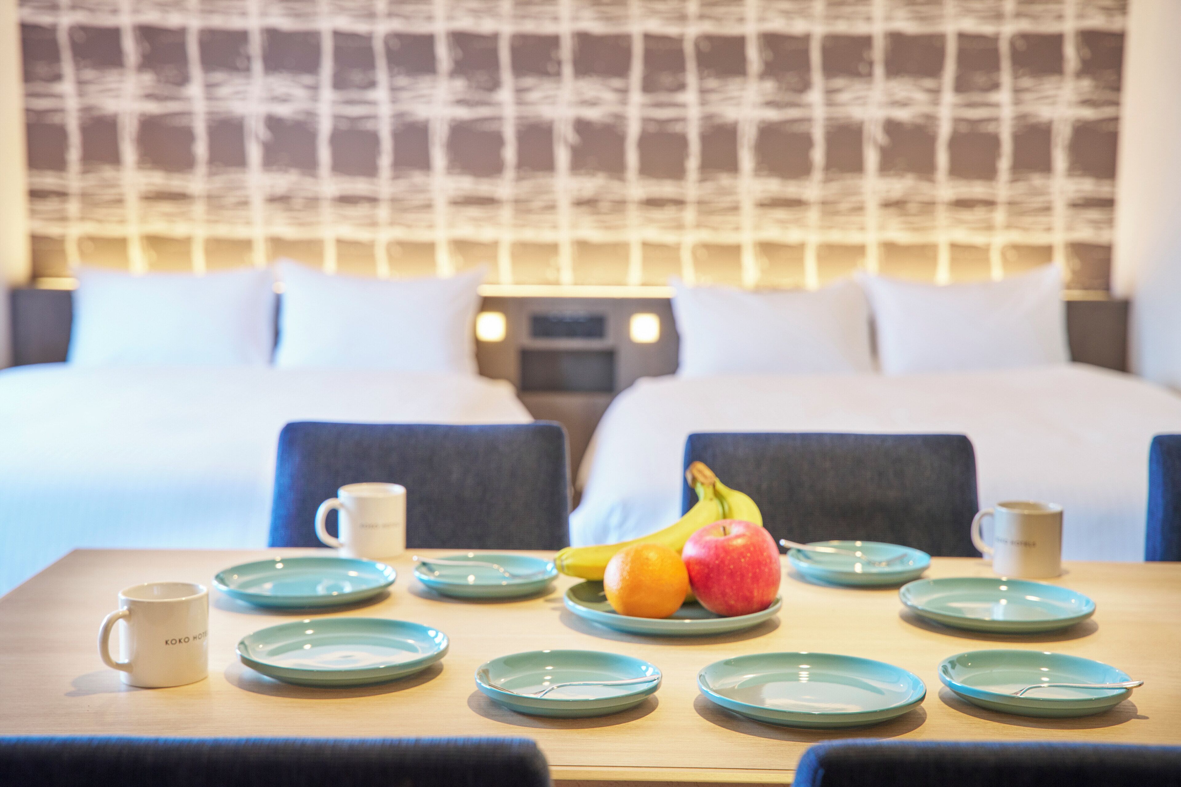 A hotel room with a neatly made bed, a breakfast table with plates, cups, and fruit.