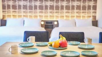 A hotel room with a neatly made bed, a breakfast table with plates, cups, and fruit.