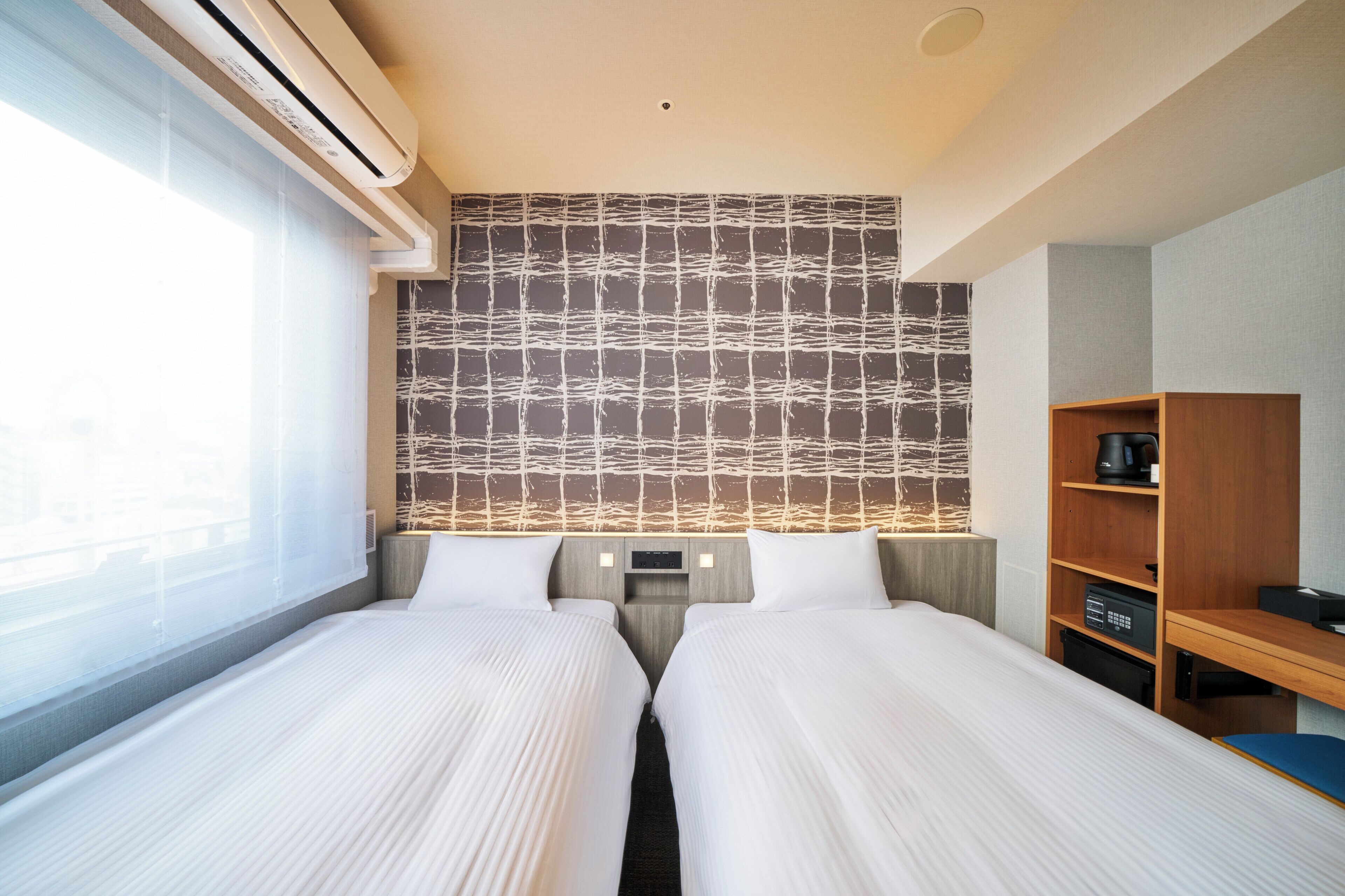 A hotel room with two beds, a wooden desk, a TV, and a wall with a textured pattern.