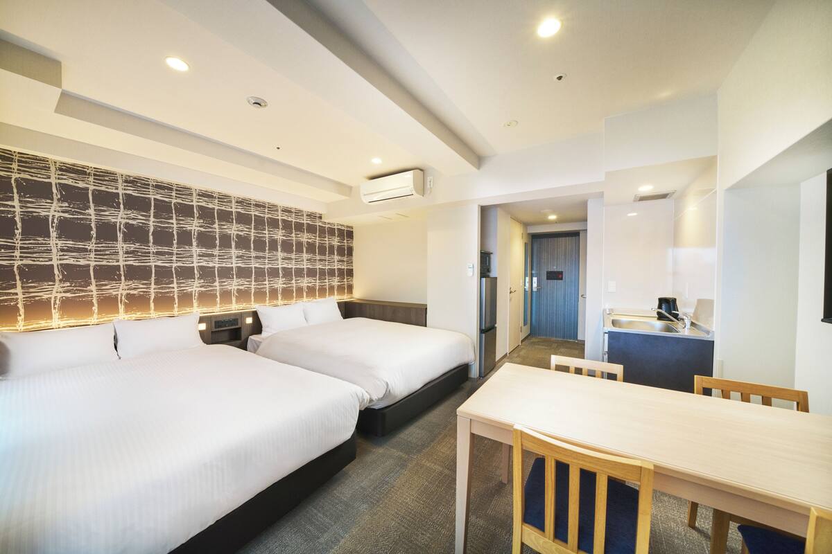 Ein Hotelzimmer mit zwei Betten, einem Esstisch und einer Küchenzeile.