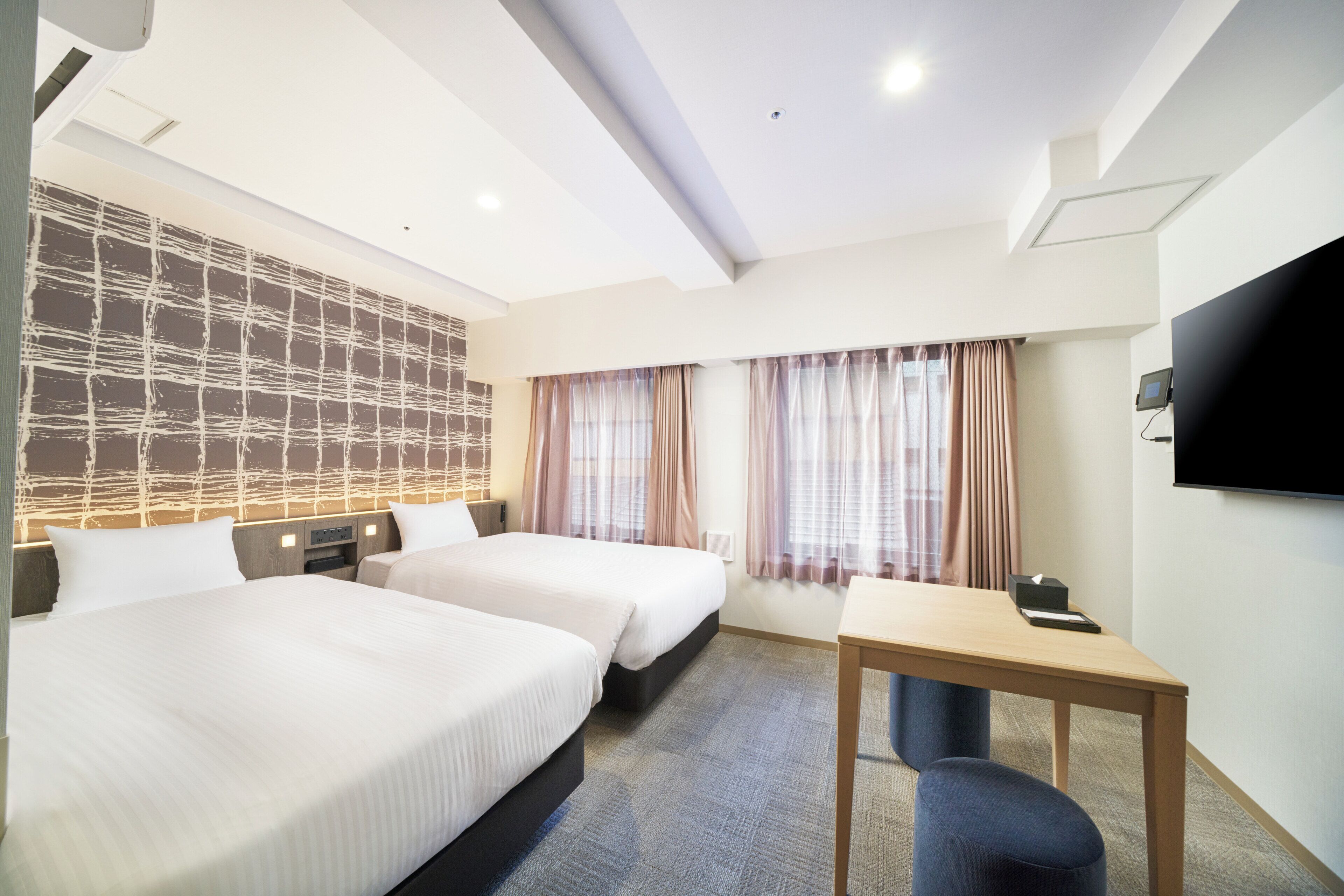 A hotel room with two beds, a desk, a TV, and a large window with curtains.