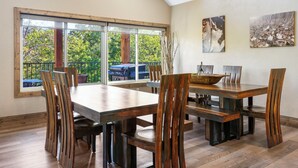 Un espace repas comprenant une grande table et des chaises, de grandes fenêtres donnant sur un paysage verdoyant, et des œuvres d’art accrochées aux murs.