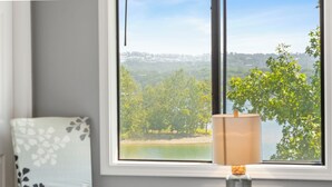 Una habitación con vista a un lago y árboles, una lámpara sobre una mesa y una silla con estampado floral.