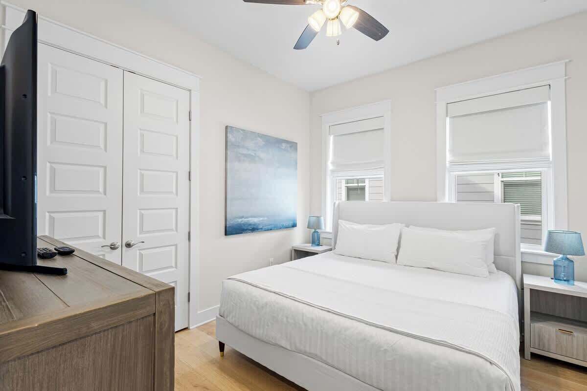 Une chambre à coucher avec un lit, un téléviseur posé sur une commode, un ventilateur de plafond et un tableau accroché au mur.
