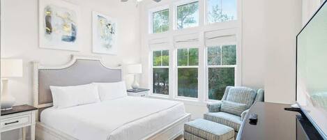 A bedroom with a bed, a ceiling fan, a window with blinds, a chair, and a TV.