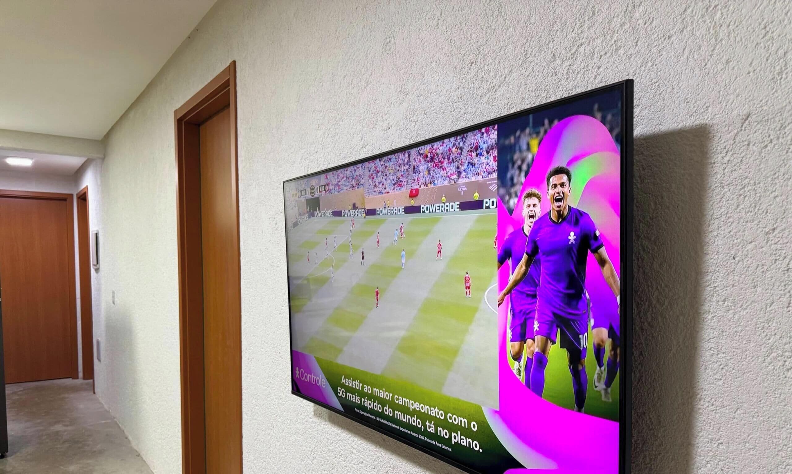 A wall-mounted TV displaying a soccer match with players in purple jerseys.