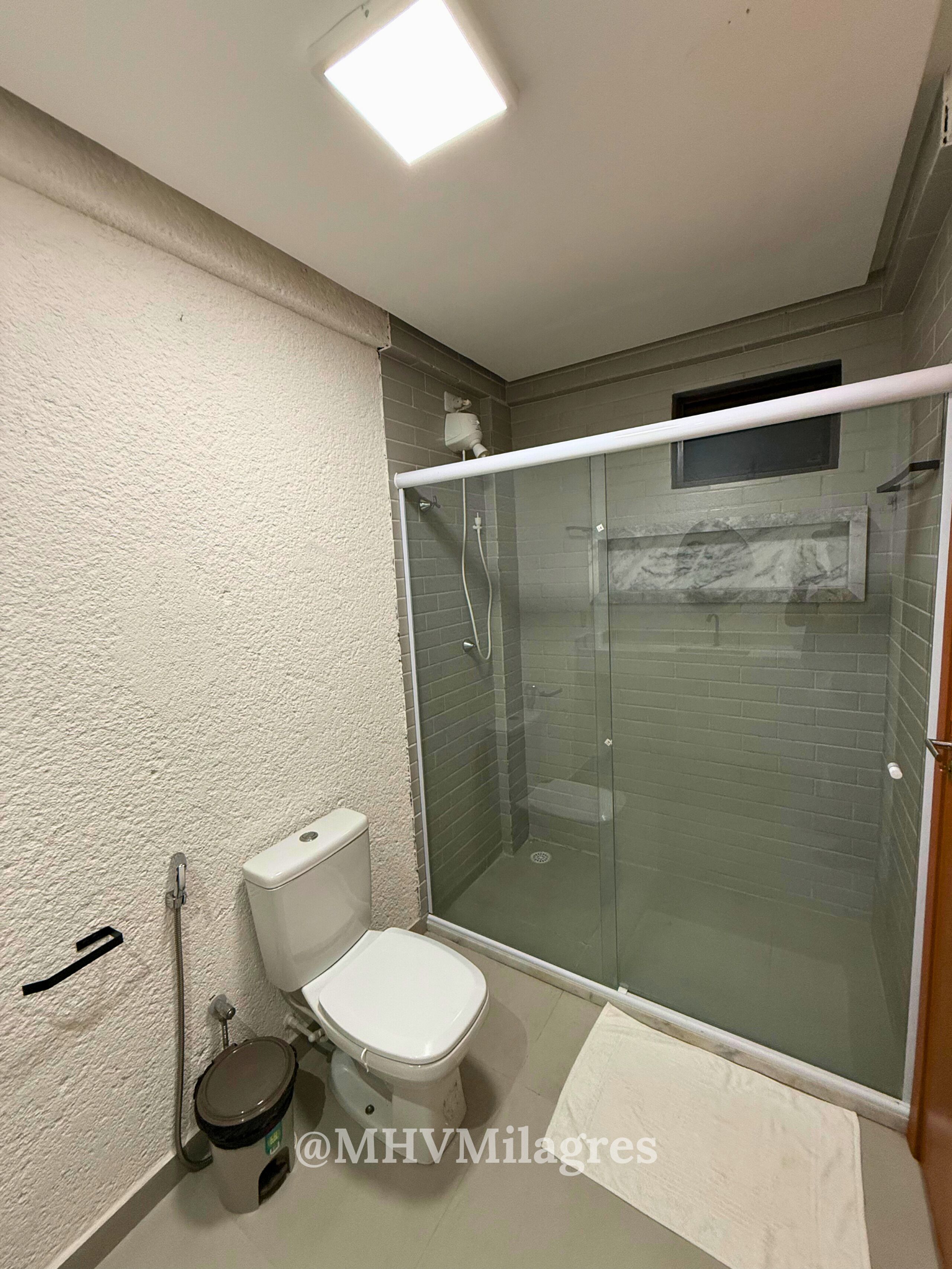 Casa de banho com sanita, cabine de duche em vidro e lavatório branco.