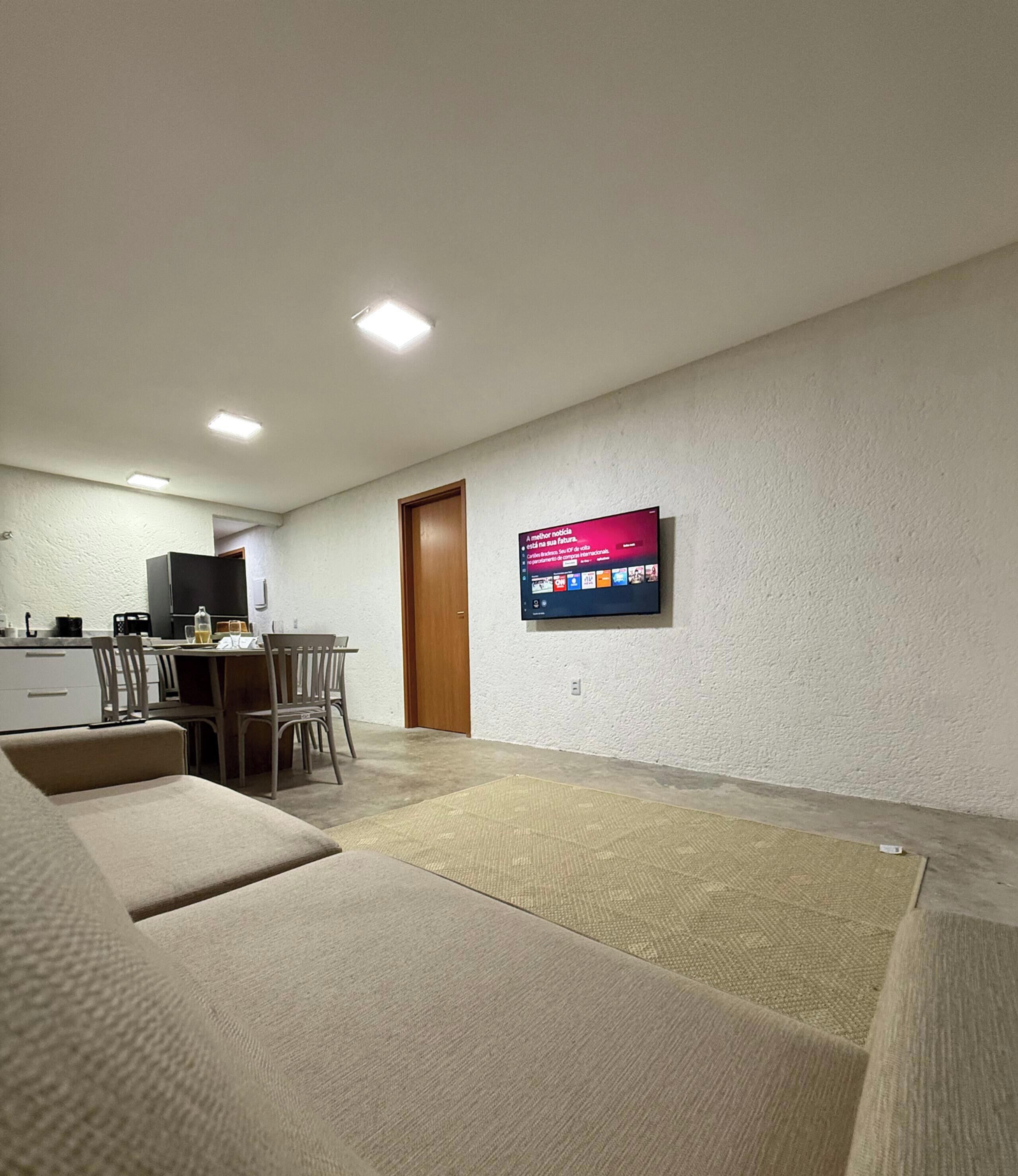 Ein Wohnzimmer mit einer Couch, einem an der Wand montierten Fernseher und einem Essbereich mit Stühlen und einem Tisch.