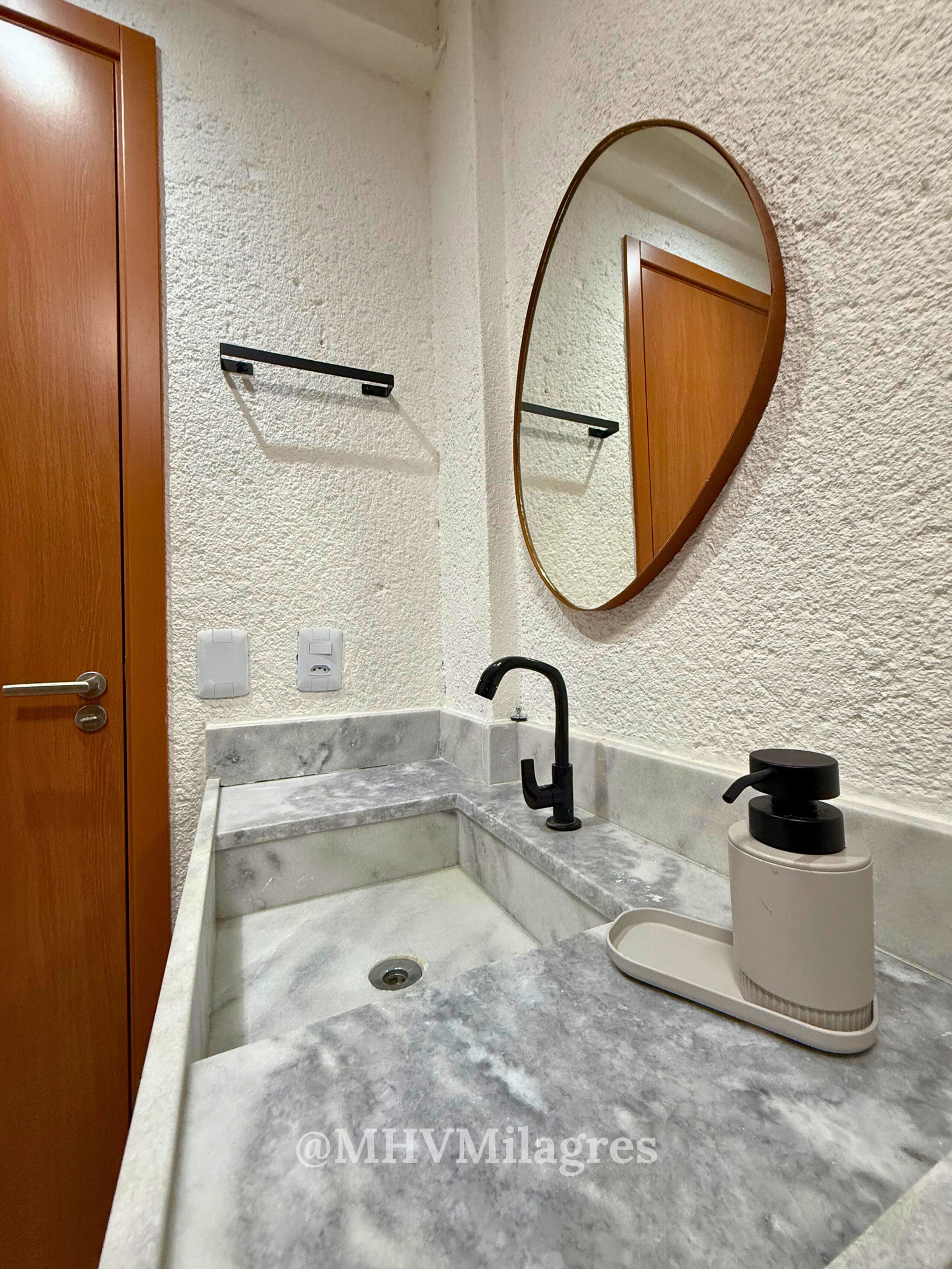 A bathroom with a marble sink, a black faucet, a mirror, and a wooden door.
