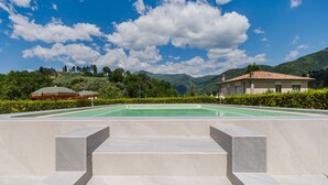 Una piscina con escalones que la bordean, rodeada de vegetación y con una montaña al fondo.