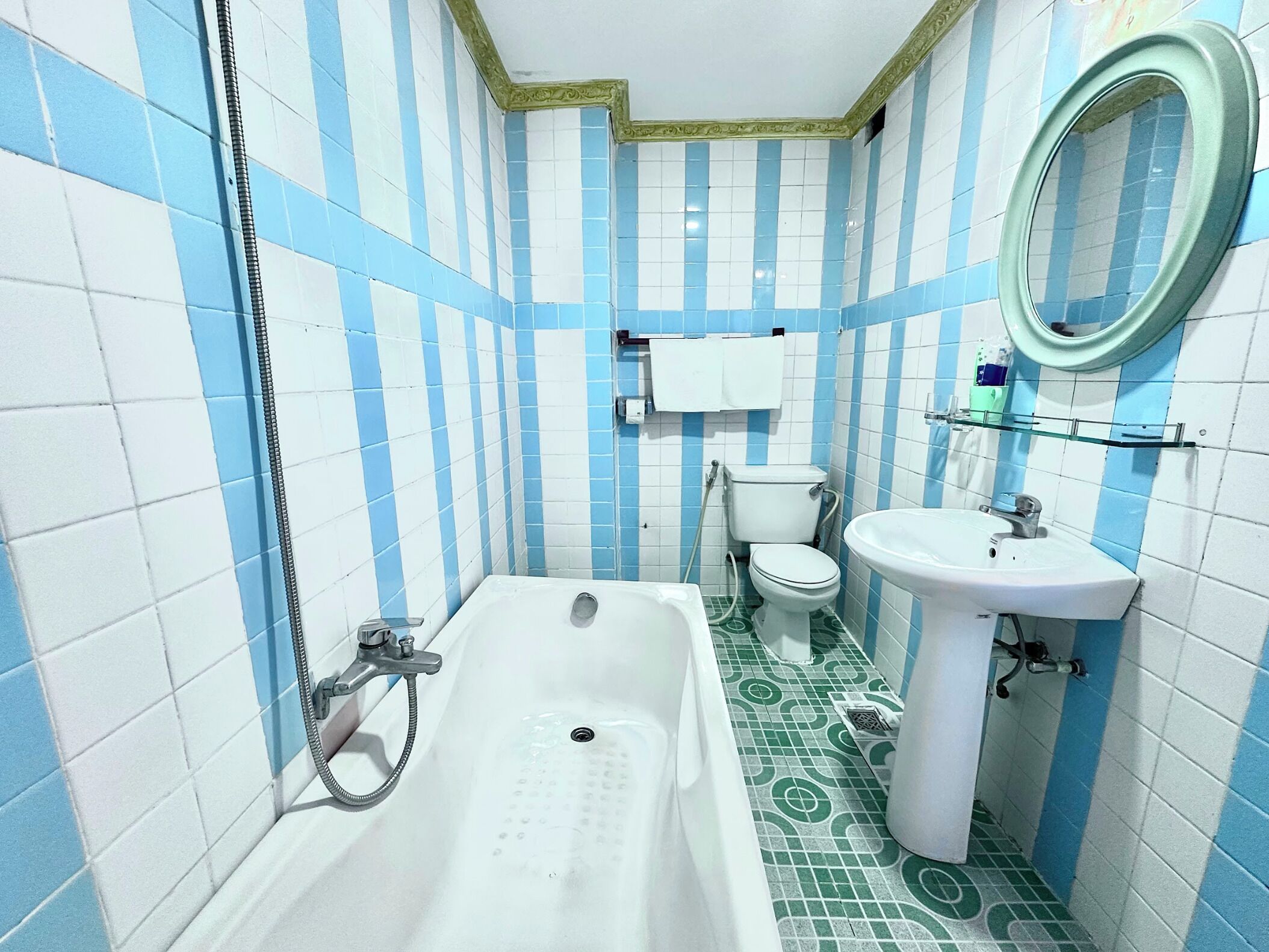 Baño con bañera, inodoro y lavamanos, con azulejos azul y blanco y piso estampado en tonos verdes.