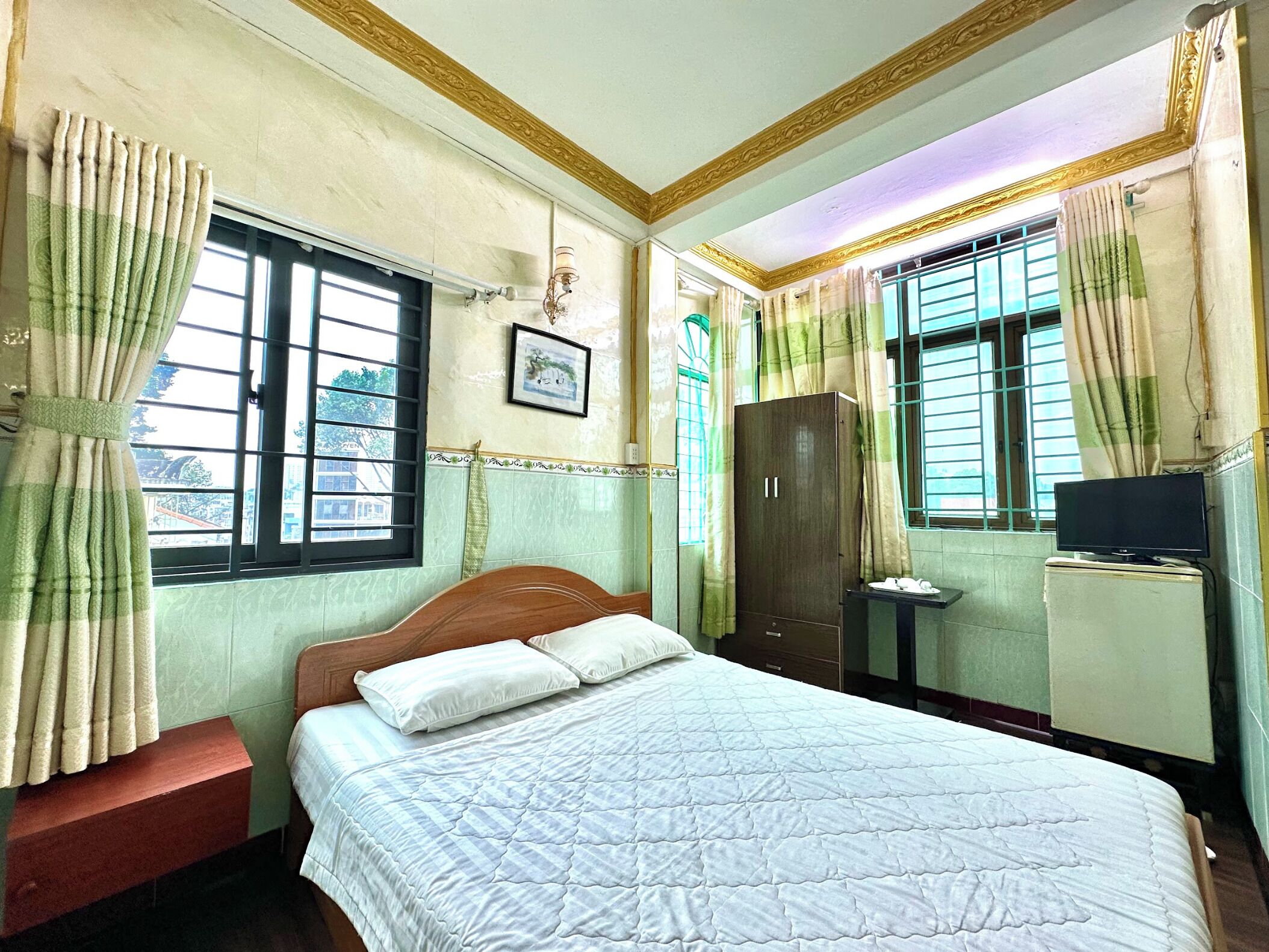 A bedroom with a bed, a wardrobe, a television, and a window with curtains.