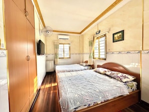 Une chambre avec deux lits, une armoire, un téléviseur et une fenêtre avec des rideaux.