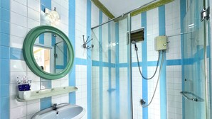 Une salle de bain avec une douche à parois de verre, un lavabo blanc et un miroir avec un cadre vert.
