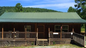 A rustic cabin with a green metal roof, wooden deck, and a sign indicating 'Cabin Lodge'. - Laurel Lodge-Devil`s Bathtub/Nat Tunnel (DUFFIELD)