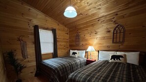 A cabin-style room with two beds, wooden walls, a window with blinds, a lamp, and a potted plant. - Laurel Lodge-Devil`s Bathtub/Nat Tunnel (DUFFIELD)