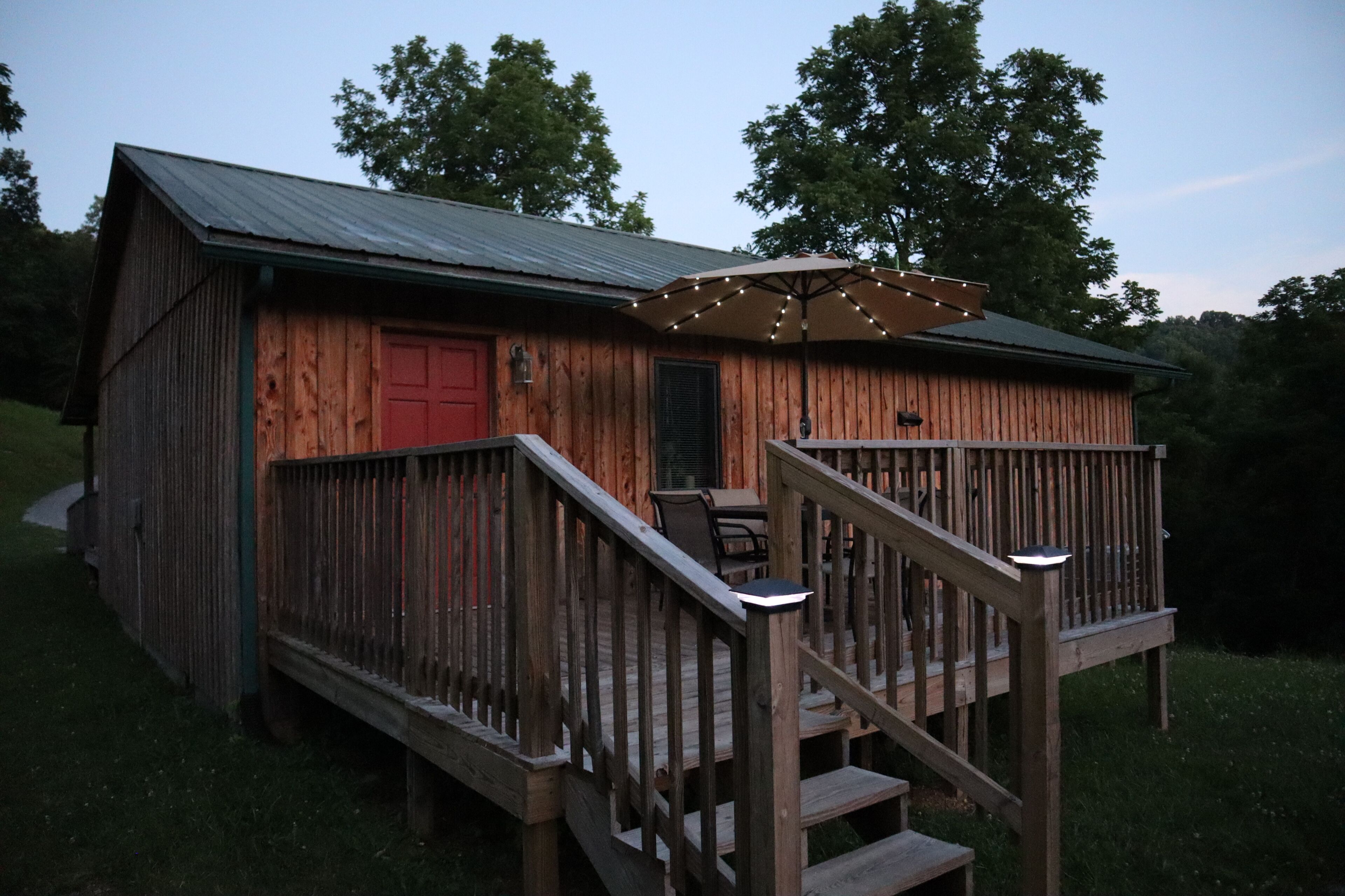 A wooden cabin with a red door, a covered deck with stairs, and a metal roof.