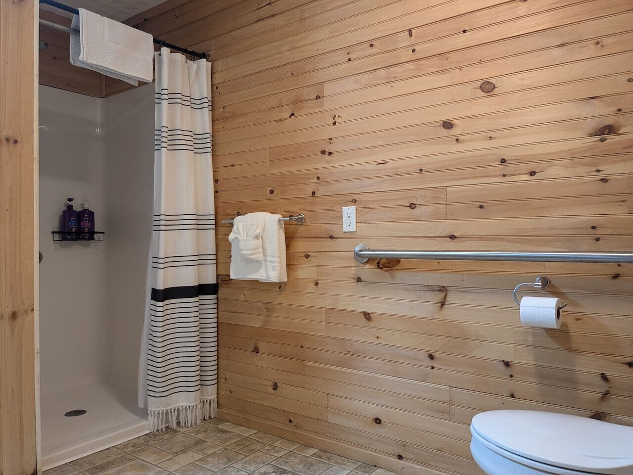 A wooden-paneled bathroom with a shower, toilet, and towel rack.