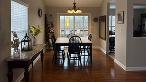 A dining area with a wooden table and chairs, a chandelier, and a view through large windows. - NEW LISTING! Home with a POOL, PARK, and close to Arrowhead & Kauffman! (Blue Springs)