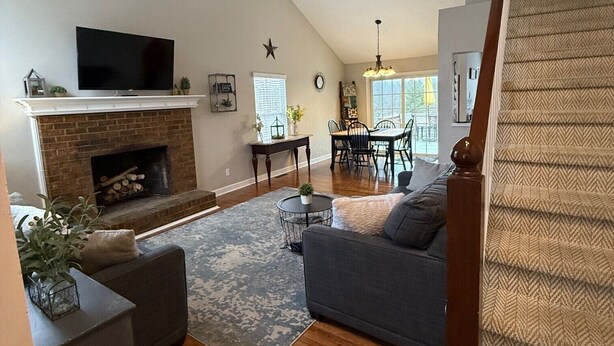 A spacious living room with a fireplace, a television, a dining area, and a staircase. - NEW LISTING! Home with a POOL, PARK, and close to Arrowhead & Kauffman! (Blue Springs)