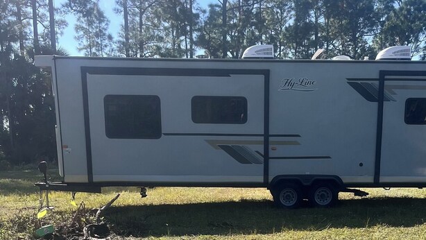 A Hy-Line RV parked on grass with a trailer hitch, windows, and a door. - Cozy RV in Palm Bay, FL with pool access! (Palm Bay)