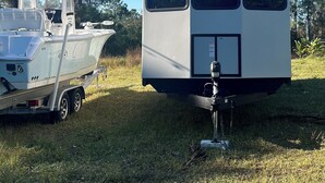 A white RV with "Hy-Line" branding parked on grass, a boat trailer attached, and a clear blue sky in the background. - Cozy RV in Palm Bay, FL with pool access! (Palm Bay)