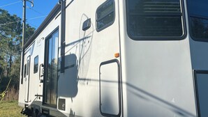 A white RV with a side door, a small window, and a logo on the side. - Cozy RV in Palm Bay, FL with pool access! (Palm Bay)