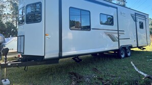 A large RV with a sliding door, multiple windows, and a flatbed trailer attached. - Cozy RV in Palm Bay, FL with pool access! (Palm Bay)