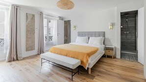 Une chambre moderne avec un grand lit, un banc, une douche et un balcon avec des rideaux.