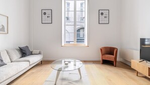 A modern living room with a sofa, a glass coffee table, a wooden cabinet, and a TV. - Blueground | Le Marais, elev & w/d, nr Pompidou (Paris)