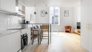 A modern kitchen with white cabinets, a coffee machine, and a small dining area with stools. - Blueground | Le Marais, elev & w/d, nr Pompidou (Paris)