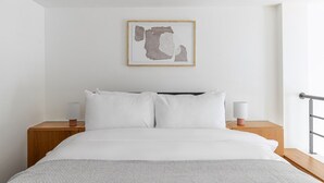 A modern hotel room with a large bed, white bedding, two bedside tables with lamps, and a minimalist artwork on the wall. - Blueground | Le Marais, elev & w/d, nr Pompidou (Paris)