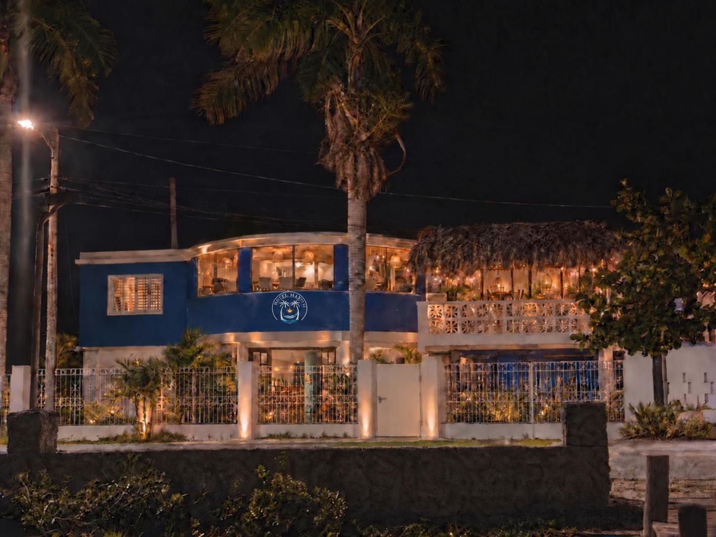 A hotel with a blue facade, a visible logo, and a thatched roof structure.