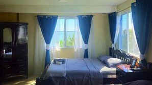 A bedroom with a bed, a dresser, and a window with curtains.