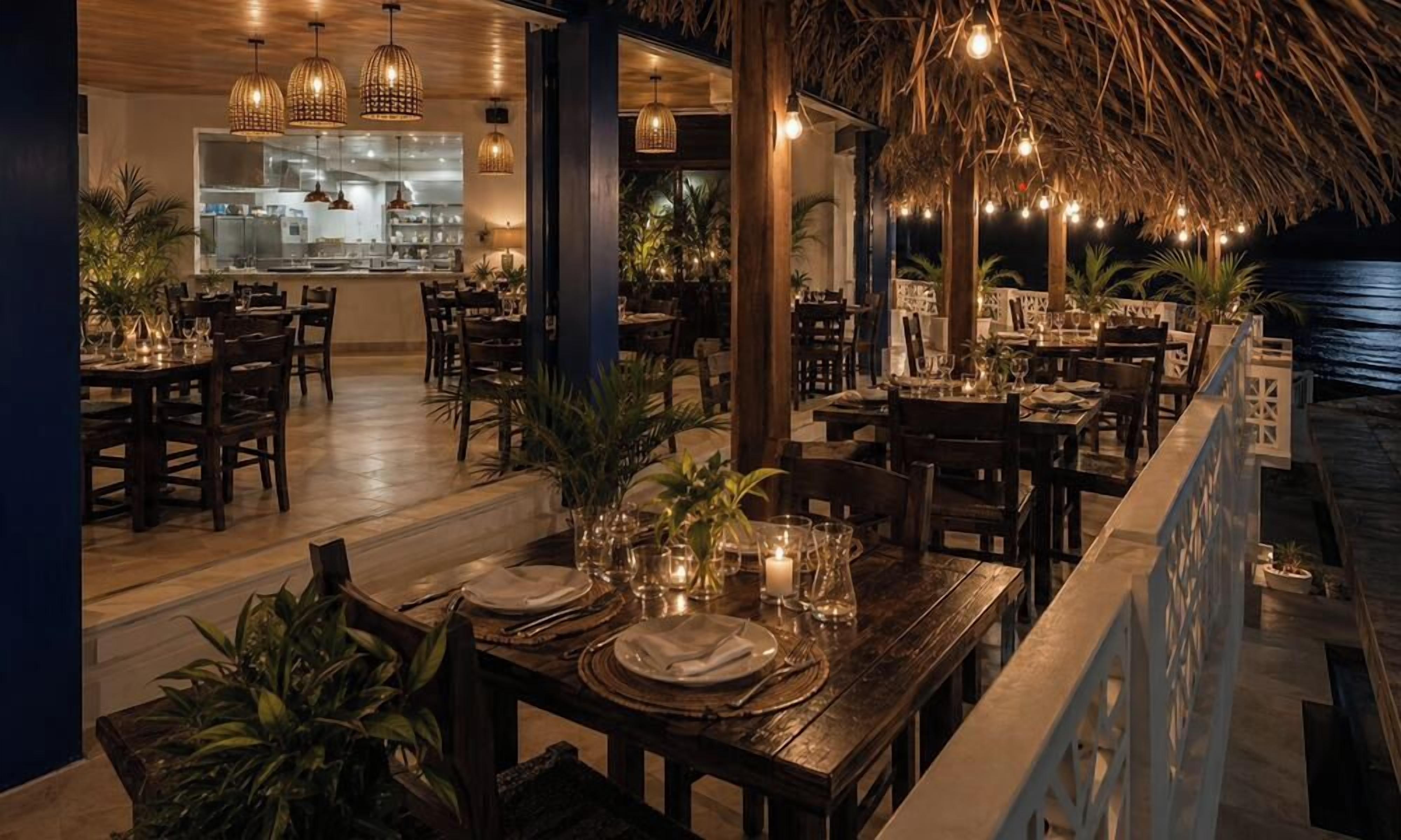 Un restaurant avec des tables et des chaises en bois, un coin bar et un toit de chaume.