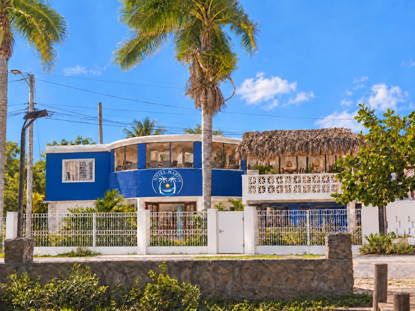 Un edificio azul con una palmera y una estructura de techo de paja, identificado como 'Hotel Martin'.