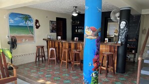 A bar area with wooden stools, a large pillar with a sea turtle mural, and a beach mural on the wall.