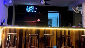 A bar area with wooden stools, a ceiling fan, and a television screen.