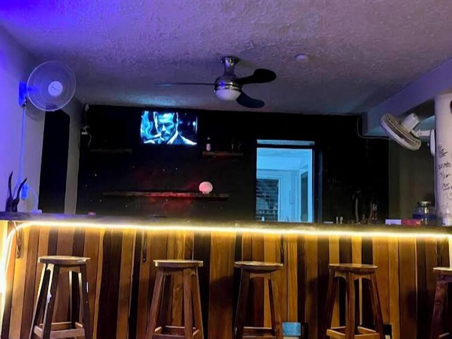A bar area with wooden stools, a ceiling fan, and a television screen.