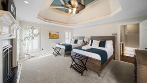 Ein Schlafzimmer mit zwei Betten, einem Deckenventilator, einem Kamin und einem großen Fenster mit Jalousien.