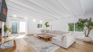 Una sala moderna con un sofá seccional, una mesa de centro de madera y un tapete estampado. Se ve un ventanal con vistas a zonas verdes.