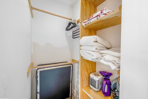 A laundry room with a metal drying rack, shelves with folded towels, a portable heater, and a vacuum cleaner.