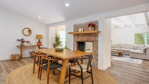 Un comedor con mesa y sillas de madera, chimenea de ladrillo y vista al exterior.