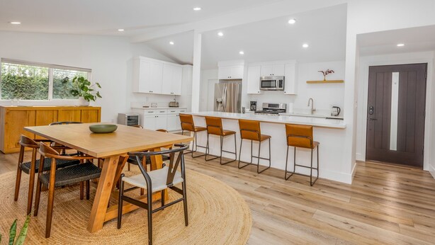 Una cocina moderna con armarios blancos, una mesa de comedor de madera y una zona de bar.