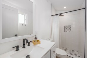 Un baño moderno con un lavabo blanco, un espejo, un inodoro y una zona de ducha.